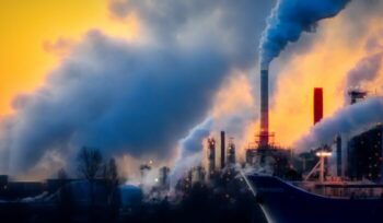 A boat in front of a factory emitting smoke|acoop