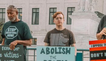 A man holding a sign says "Abolish the Death Penalty"