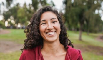 Portrait of native american woman smiling on camera with city park in background - Indigenous girl outdoor